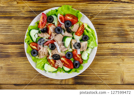 Tasty tuna salad with lettuce, black olives and fresh vegetables on wooden table. Top view Tasty tuna salad with lettuce, black olives and fresh vegetables on wooden table. Top view 127599472