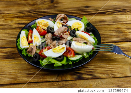 Tasty tuna salad with lettuce, black olives, eggs and fresh vegetables on wooden table Tasty tuna salad with lettuce, black olives, eggs and fresh vegetables on wooden table 127599474