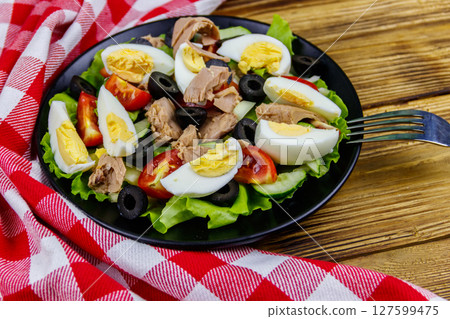 Tasty tuna salad with lettuce, black olives, eggs and fresh vegetables on wooden table 127599475