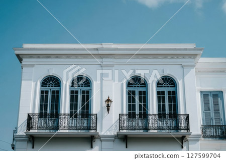 Sleek White Building Facade Rising Below Blue Sky with Elegant Arches and Balconies Sleek White Building Facade Rising Below Blue Sky with Elegant Arches and Balconies 127599704
