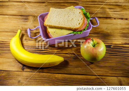 Lunch box with sandwiches, banana and apple on a wooden table Lunch box with sandwiches, banana and apple on a wooden table 127601055