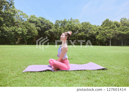 A woman doing yoga and pilates in a resort atmosphere under natural grass and blue skies A woman doing yoga and pilates in a resort atmosphere under natural grass and blue skies 127601414