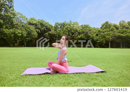 A woman doing yoga and pilates in a resort atmosphere under natural grass and blue skies A woman doing yoga and pilates in a resort atmosphere under natural grass and blue skies 127601419