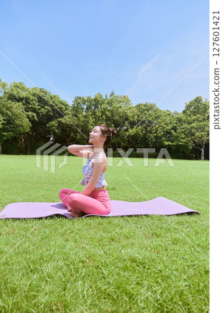 A woman doing yoga and pilates in a resort atmosphere under natural grass and blue skies A woman doing yoga and pilates in a resort atmosphere under natural grass and blue skies 127601421