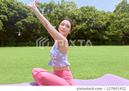 A woman doing yoga and pilates in a resort atmosphere under natural grass and blue skies 127601432