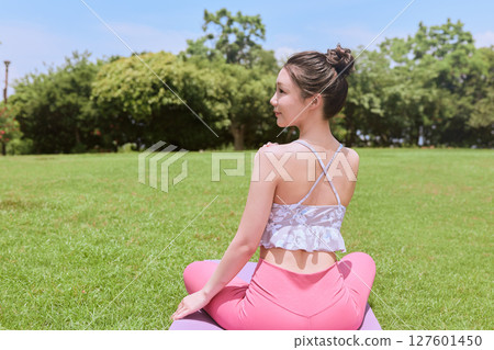 A woman doing yoga and pilates in a resort atmosphere under natural grass and blue skies A woman doing yoga and pilates in a resort atmosphere under natural grass and blue skies 127601450