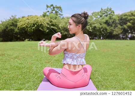 A woman doing yoga and pilates in a resort atmosphere under natural grass and blue skies 127601452