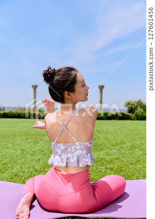 A woman doing yoga and pilates in a resort atmosphere under natural grass and blue skies 127601456