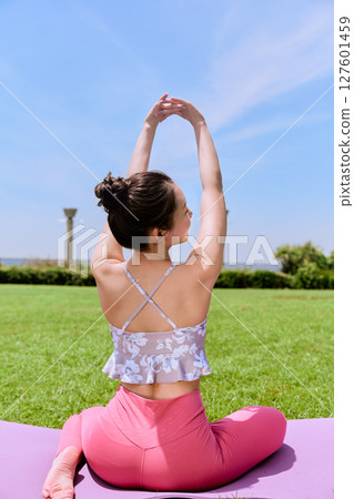 A woman doing yoga and pilates in a resort atmosphere under natural grass and blue skies 127601459