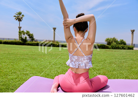 A woman doing yoga and pilates in a resort atmosphere under natural grass and blue skies A woman doing yoga and pilates in a resort atmosphere under natural grass and blue skies 127601462