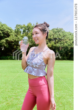 A healthy woman hydrating after yoga on natural grass under the blue sky 127601478