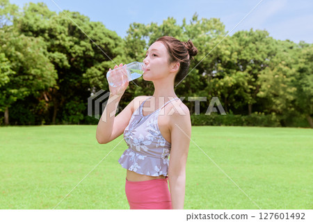 一位健康的女性在藍天下的天然草地上做完瑜伽後補充水分 一位健康的女性在藍天下的天然草地上做完瑜伽後補充水分 127601492