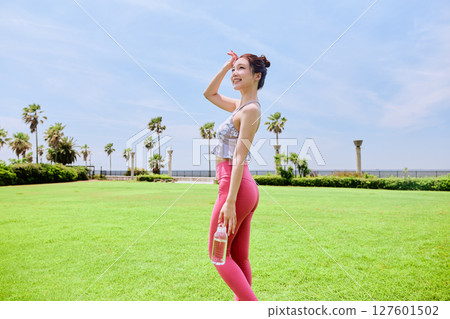 A healthy woman hydrating after yoga on natural grass under the blue sky 127601502