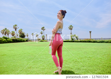 A healthy woman hydrating after yoga on natural grass under the blue sky 127601504