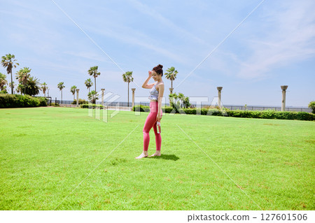 A healthy woman hydrating after yoga on natural grass under the blue sky A healthy woman hydrating after yoga on natural grass under the blue sky 127601506