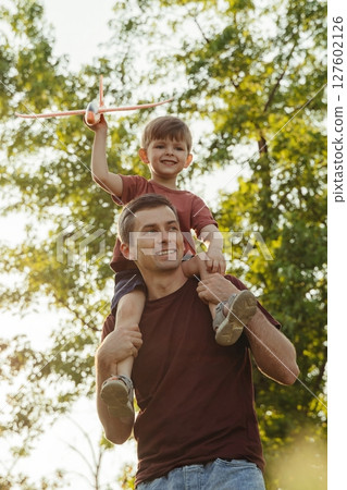 A happy father carries his joyful son on his shoulders in a park at sunset. A happy father carries his joyful son on his shoulders in a park at sunset. 127602126