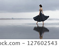 Woman in a black dress is walking on a beach 127602543