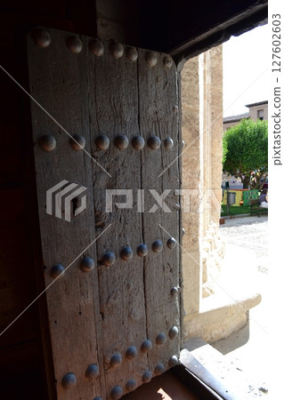 Historic wooden doorway leading to a sunlit courtyard in Brihuega, Spain. Iglesia de San Felipe. Church Saint Felipe in Brihuega, Guadalajara, Spain. Open door in the temple 127602603