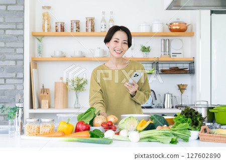 Middle-aged housewife holding a smartphone in the kitchen Middle-aged housewife holding a smartphone in the kitchen 127602890