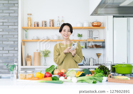 Middle-aged housewife holding a smartphone in the kitchen 127602891