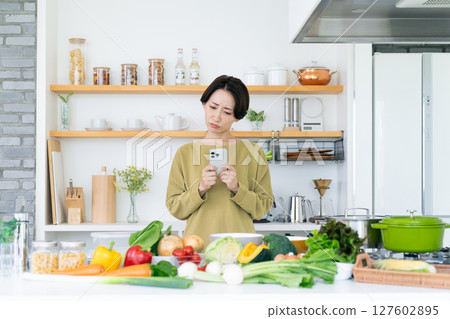 Middle-aged housewife holding a smartphone in the kitchen Middle-aged housewife holding a smartphone in the kitchen 127602895