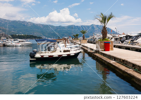 Motorboat moored in scenic marina with mountain background. Coastal lifestyle, nautical leisure, and summer tourism on waterfront. Motorboat moored in scenic marina with mountain background. Coastal lifestyle, nautical leisure, and summer tourism on waterfront. 127603224