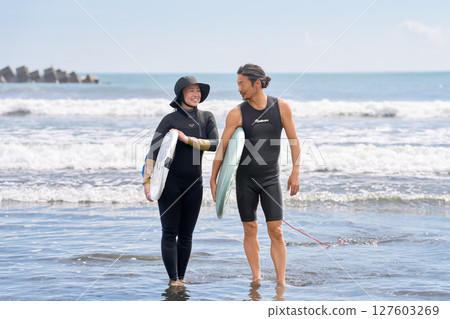 兩個男人和女人並肩站著，面帶微笑，手裡拿著衝浪板 127603269