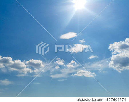 Bright blue sky with fluffy white clouds and radiant sun shining in clear atmosphere Bright blue sky with fluffy white clouds and radiant sun shining in clear atmosphere 127604274