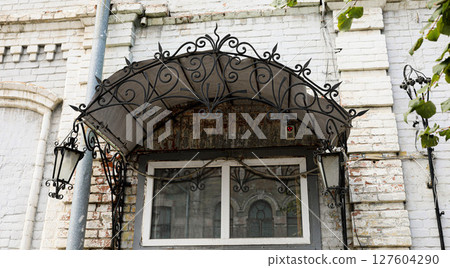 Ornate wrought iron awning above window with vintage lanterns on brick wall exterior 127604290