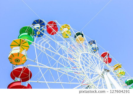Colorful ferris wheel against a clear blue sky, showcasing vibrant gondolas and structure 127604291
