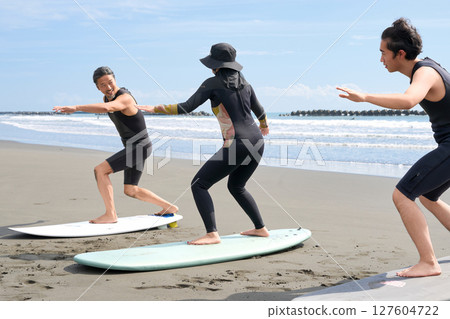 Young people and instructors experiencing surfing on the beach Surfing school image 127604722