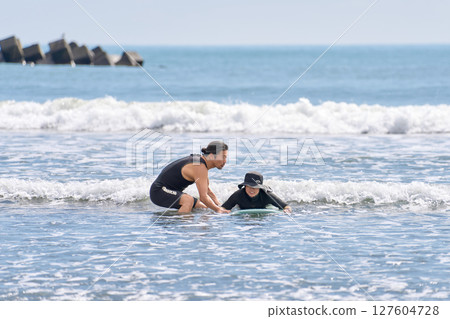 A woman trying surfing and an instructor teaching her 127604728