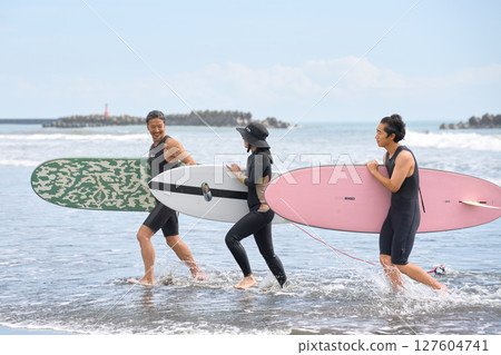 衝浪後，三名男子和女子微笑著返回海灘 127604741