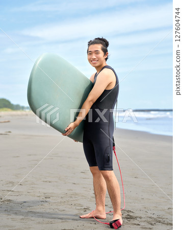 Smiling young man holding a surfboard 127604744