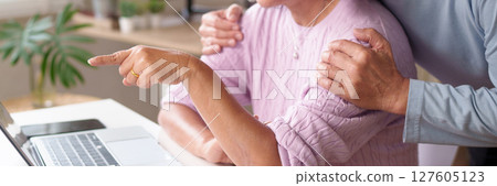 Affectionate Older Couple Pointing at Laptop Screen, Senior Couple Bonding at Home, Hands Together, Love and Support, Retirement Lifestyle, Aging Gracefully 127605123