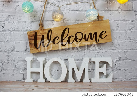 Welcome Home alphabet letters and wooden signboard hanging on white brick wall background Welcome Home alphabet letters and wooden signboard hanging on white brick wall background 127605345