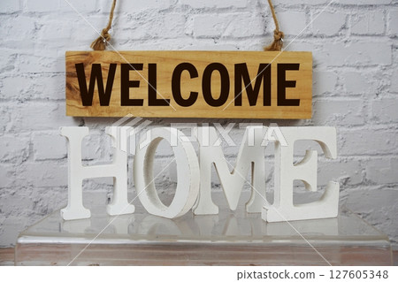 Welcome Home alphabet letters and wooden signboard hanging on white brick wall background 127605348