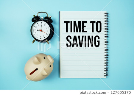 Time to Saving text on notebook paper and piggy bank and alarm clock on blue background 127605370