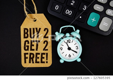 Buy 2 Get 2 Free! text on price tag with alarm clock and calculator on black background 127605395