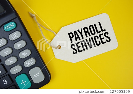 Payroll Services text on price tag with alarm clock and calculator on yellow background 127605399