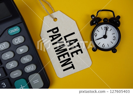 Late Payment text on price tag with alarm clock and calculator on yellow background Late Payment text on price tag with alarm clock and calculator on yellow background 127605403