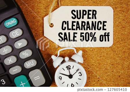 Clearance Sale 50% Off text on price tag with alarm clock and calculator on cork board background 127605410