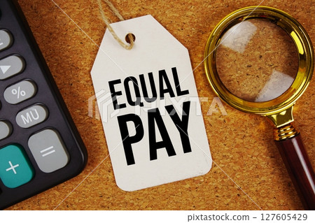 Equal Pay text on price tag with magnifying glass and calculator on cork board background Equal Pay text on price tag with magnifying glass and calculator on cork board background 127605429
