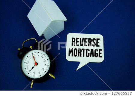 Reverse Mortgage text with alarm clock and house model top view on blue background Reverse Mortgage text with alarm clock and house model top view on blue background 127605537