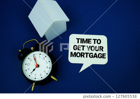 Time to Get Your Mortgage text with alarm clock and house model top view on blue background Time to Get Your Mortgage text with alarm clock and house model top view on blue background 127605538