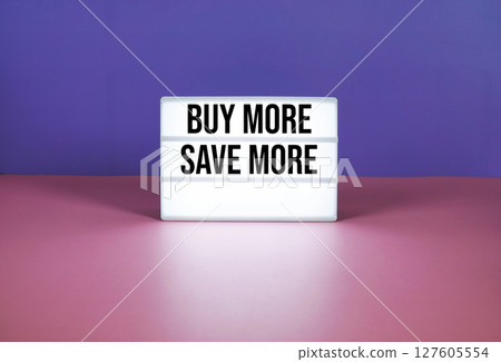 Buy More Save More text on LED lightbox on purple and pink geometric background 127605554