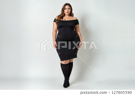 Confident plus-size woman in a black off-the-shoulder dress and knee-high socks. 127605590