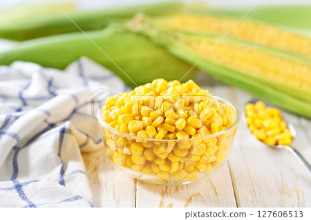 Canned young corn grain in a clear glass bowl on a white table, selective focus. 127606513