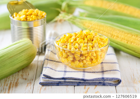 Transparent bowl with canned food maize on a light kitchen table, selective focus. Transparent bowl with canned food maize on a light kitchen table, selective focus. 127606519