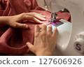 A woman sews on a sewing machine 127606926